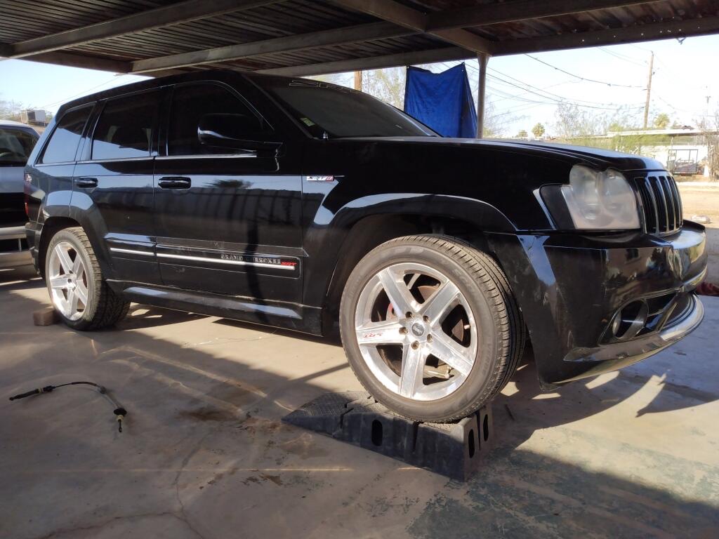 Black SRT Jeep raised on ramps under a metal carport with a shifter cable lying on the concrete in the foreground